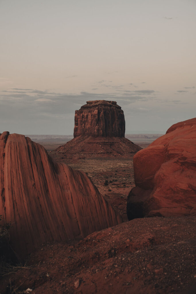 Formaciones rocosas de arenisca roja en el desierto, con un butte columnar al fondo al atardecer