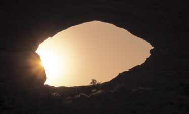 Vista desde el interior de una cueva hacia el exterior, con luz solar iluminando la boca rocosa de la caverna