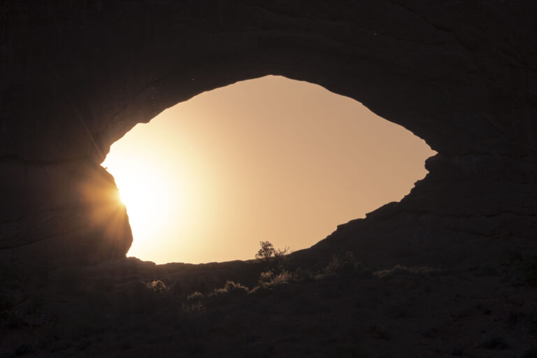 Vista desde el interior de una cueva hacia el exterior, con luz solar iluminando la boca rocosa de la caverna