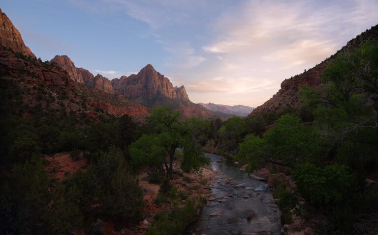 Cañón con río entre acantilados de roca roja, vegetación verde y montañas al fondo al atardecer