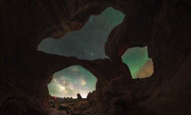 Vista desde el interior de una cueva de roca hacia el exterior, con la Vía Láctea visible en el cielo nocturno y formaciones rocosas iluminadas al amanecer