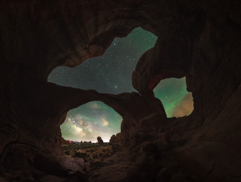 Vista desde el interior de una cueva de roca hacia el exterior, con la Vía Láctea visible en el cielo nocturno y formaciones rocosas iluminadas al amanecer
