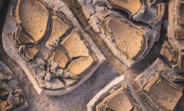Fotografía aérea de estructuras minerales fracturadas con patrones geométricos y tonos ocres y terrosos.
