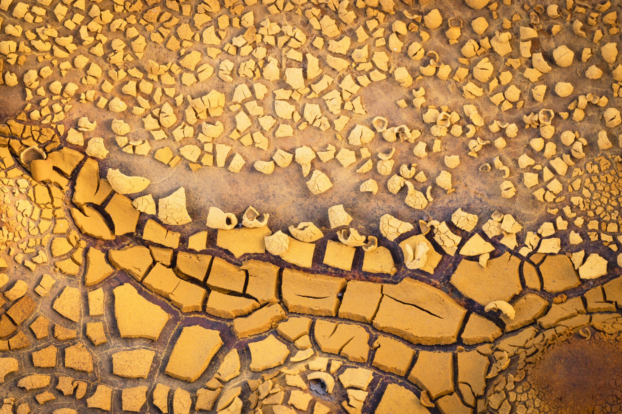 Fotografía de superficie mineral con patrones de desecación y fragmentación en tonos amarillos y ocres.