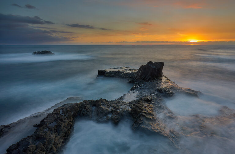 Rocas basálticas en el océano al amanecer con aguas turquesas y cielo dorado en la costa norte española