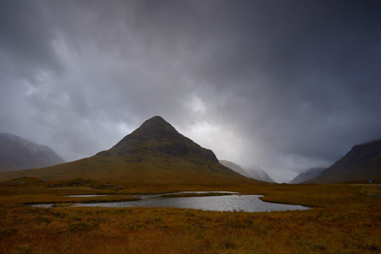 Montaña cónica con pico nevado, valle de tundra y laguna en paisaje escocés nublado