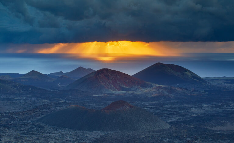 Volcanes de Lanzarote al amanecer con rayos solares atravesando nubes oscuras sobre el océano