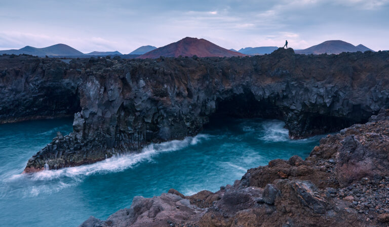 Acantilados de basalto negro frente a aguas turquesas con volcanes al fondo en Lanzarote