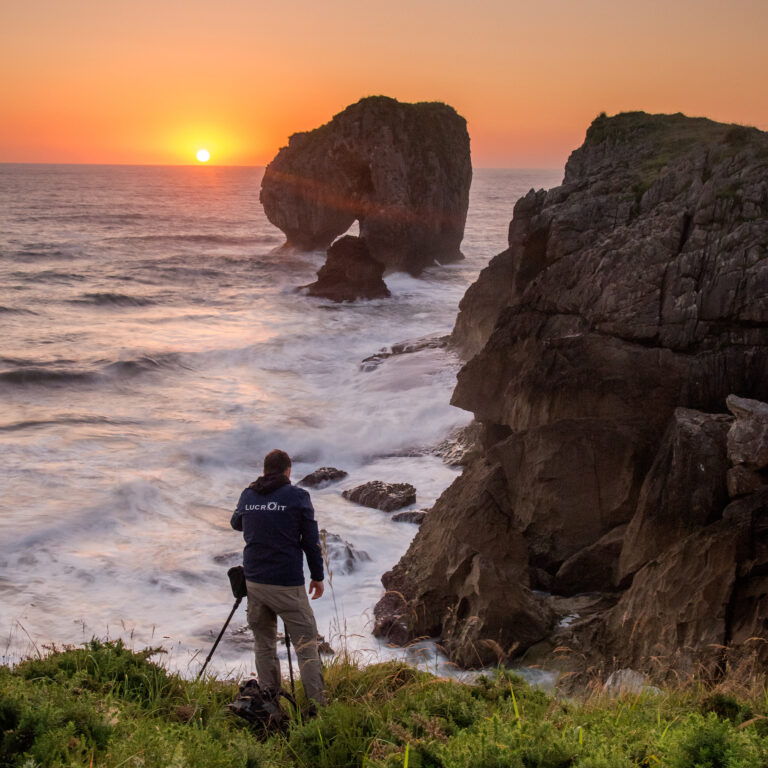 Senderista en acantilado rocoso al atardecer frente a formaciones de roca en la costa norte española