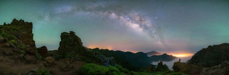 Vía Láctea sobre panorámica nocturna de La Palma con andenes de piedra, mar de nubes y volcanes iluminados al atardecer