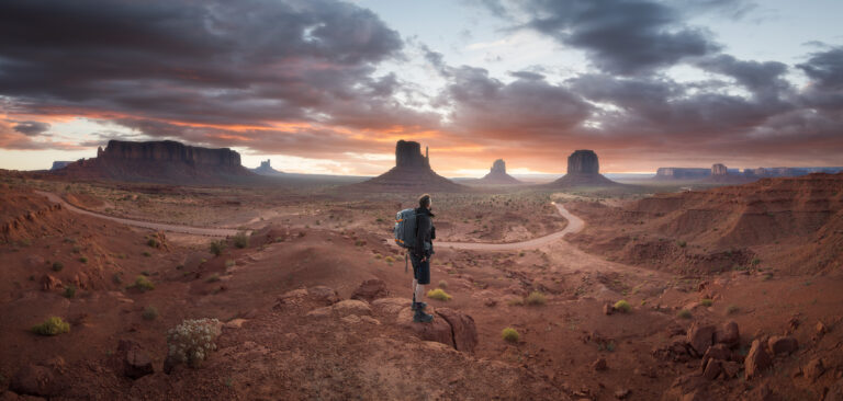 Senderista con mochila observa los monumentos de Monument Valley al atardecer