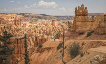 Cañón de Bryce con formaciones de hoodoos de roca roja y senderista en el valle, montañas al fondo