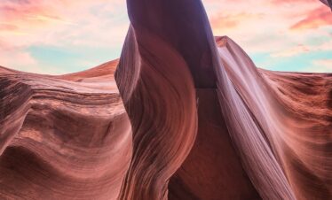 Cañón de arenisca roja con formaciones rocosas ondulantes y cielo rosa al atardecer