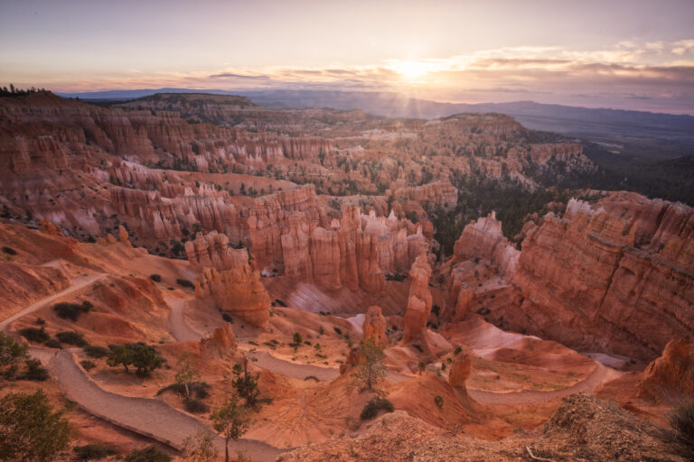Amanecer en Bryce Canyon con formaciones rocosas de arenisca roja y bosque de coníferas al fondo