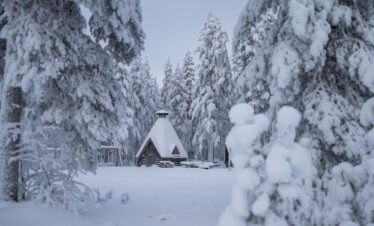 Cabaña de madera con techo nevado rodeada de abetos cubiertos de nieve en bosque de Laponia