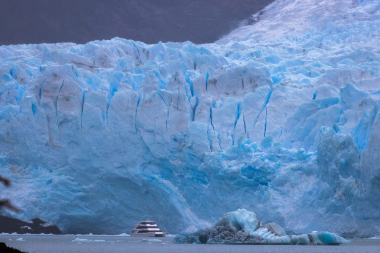Glaciar Perito Moreno con enorme pared de hielo azul, bloques desprendidos flotando en laguna glaciar y embarcación de expedición al pie