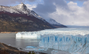 Glaciar Perito Moreno en lago Argentino con montaña nevada de fondo bajo cielo nublado
