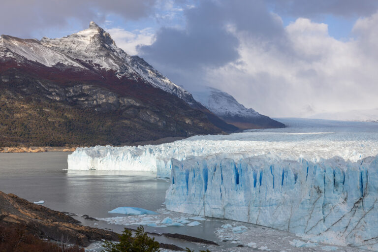 Glaciar Perito Moreno en lago Argentino con montaña nevada de fondo bajo cielo nublado