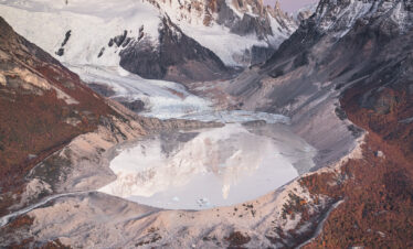Valle glaciar con lago de fusión, picos nevados y bosque de alerces en otoño, Patagonia