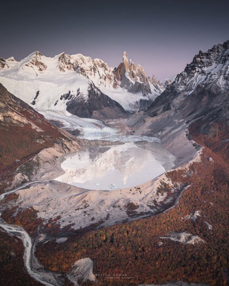 Valle glaciar con lago de fusión, picos nevados y bosque de alerces en otoño, Patagonia