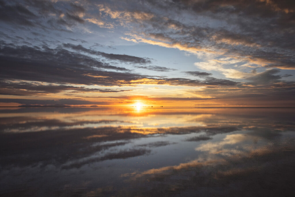 Atardecer en el Salar de Uyuni con el sol reflejado en la superficie plana del agua salada y nubes doradas en el cielo