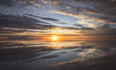 Atardecer en el Salar de Uyuni con el sol reflejado en la superficie plana del agua salada y nubes doradas en el cielo