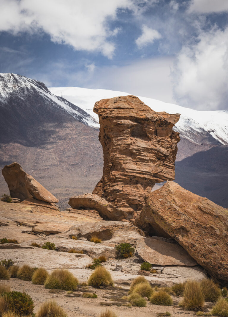 Formación rocosa erosionada en primer plano con montañas nevadas al fondo en el Salar de Uyuni, Bolivia