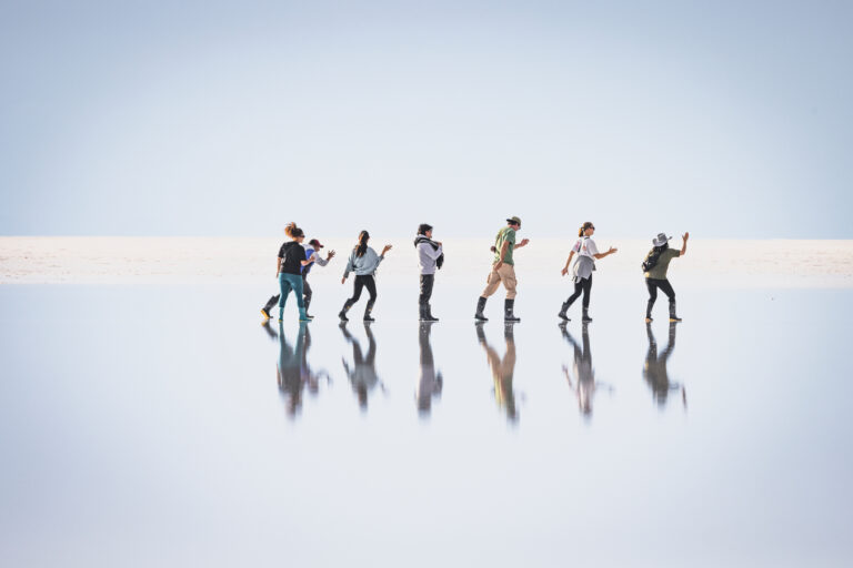 Seis expedicionarios corriendo en línea sobre el espejo del Salar de Uyuni, reflejándose en el agua salada
