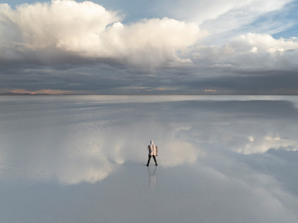 Viajero en el vasto espejo de agua del Salar de Uyuni, reflejando el cielo nublado del altiplano boliviano.