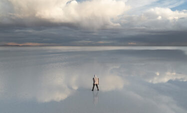 Viajero en el vasto espejo de agua del Salar de Uyuni, reflejando el cielo nublado del altiplano boliviano.