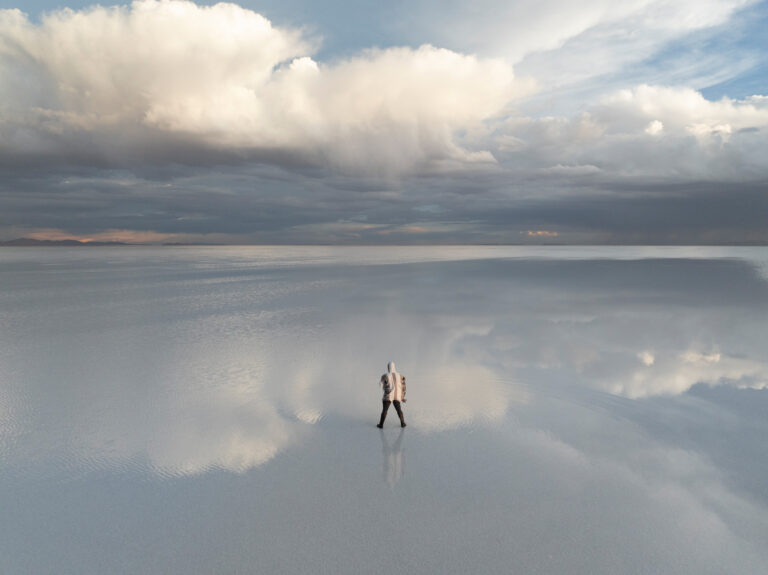 Viajero en el vasto espejo de agua del Salar de Uyuni, reflejando el cielo nublado del altiplano boliviano.
