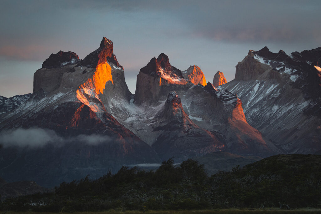 Torres del Paine iluminadas por luz dorada al atardecer, con nieves eternas y bosques de la Patagonia en primer plano