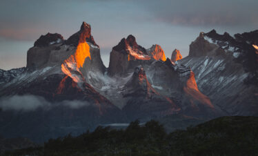 Torres del Paine iluminadas por luz dorada al atardecer, con nieves eternas y bosques de la Patagonia en primer plano