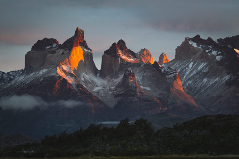 Torres del Paine iluminadas por luz dorada al atardecer, con nieves eternas y bosques de la Patagonia en primer plano