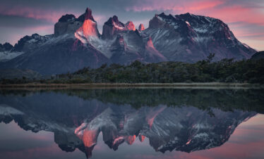 Montañas de granito con picos nevados reflejados en lago tranquilo al atardecer, Patagonia.