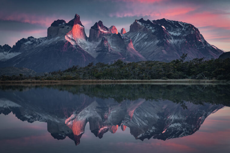 Montañas de granito con picos nevados reflejados en lago tranquilo al atardecer, Patagonia.