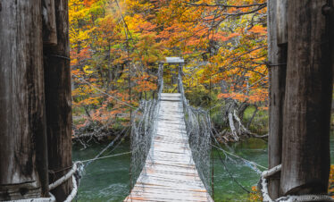 Puente colgante de madera sobre río con bosque de otoño al fondo en la Patagonia
