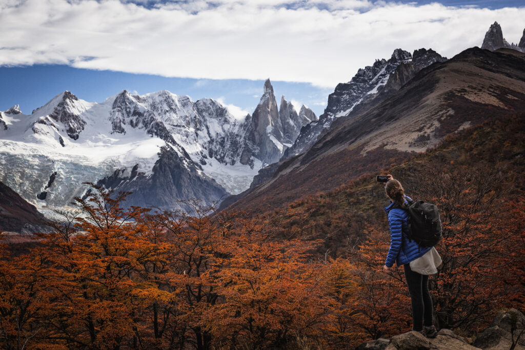 Senderista con mochila observa panorama de montañas nevadas y bosque patagónico en otoño