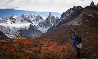 Senderista con mochila observa panorama de montañas nevadas y bosque patagónico en otoño