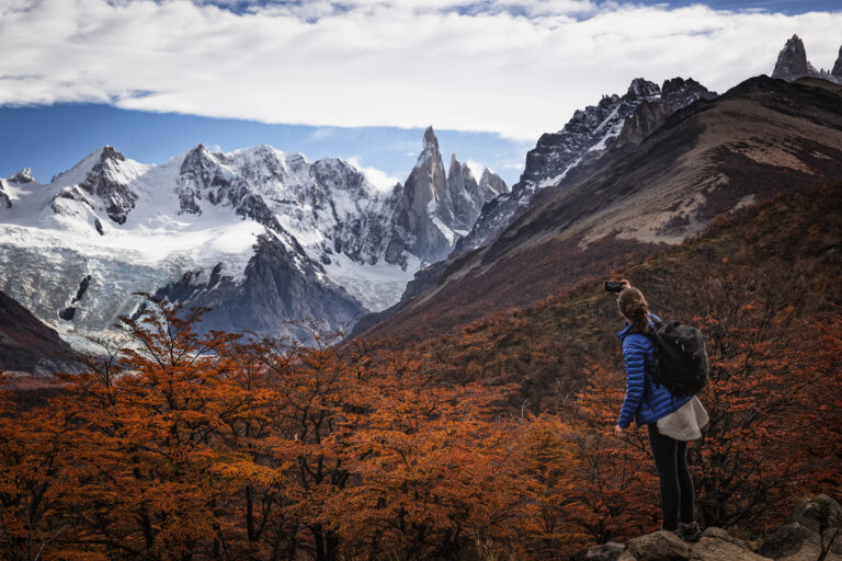 Senderista con mochila observa panorama de montañas nevadas y bosque patagónico en otoño