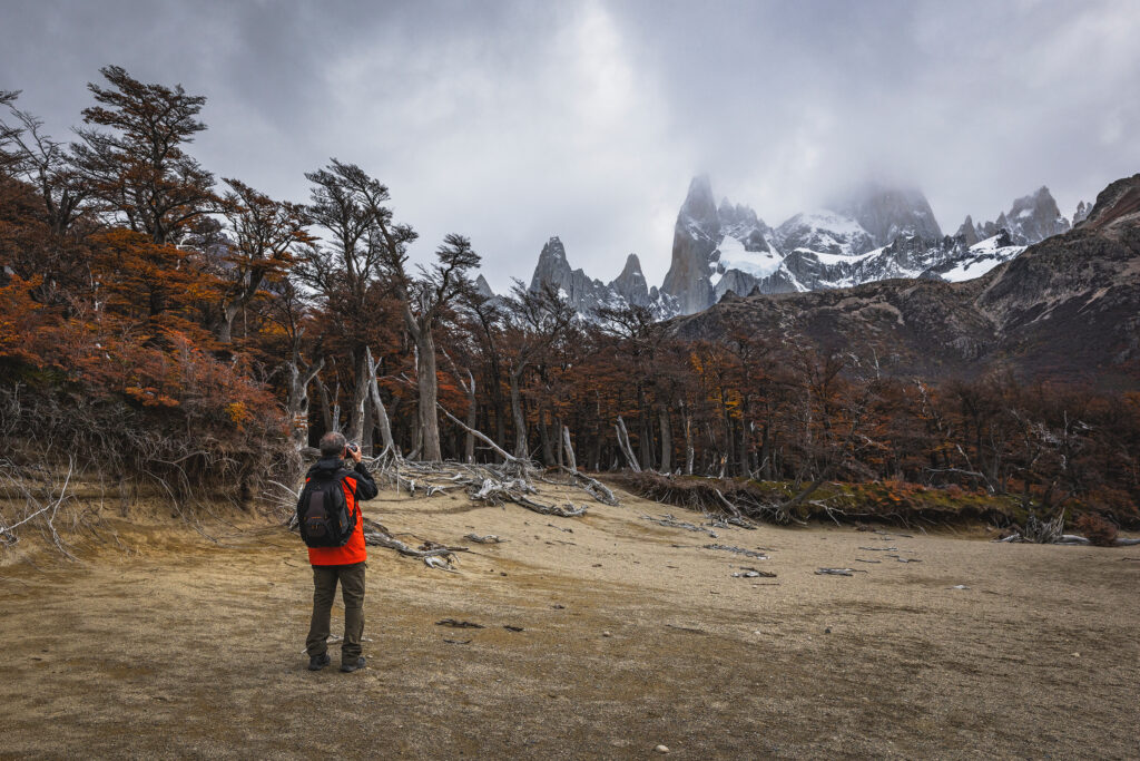 Trekker con mochila roja en valle de Patagonia, Fitz Roy nevado al fondo y bosque de lengas