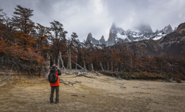 Trekker con mochila roja en valle de Patagonia, Fitz Roy nevado al fondo y bosque de lengas