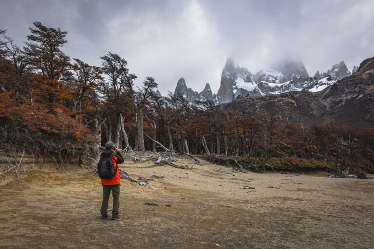 Trekker con mochila roja en valle de Patagonia, Fitz Roy nevado al fondo y bosque de lengas