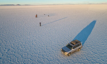 Vehículo 4x4 con sombra alargada en el Salar de Uyuni, con personas caminando en la planicie salina de Bolivia