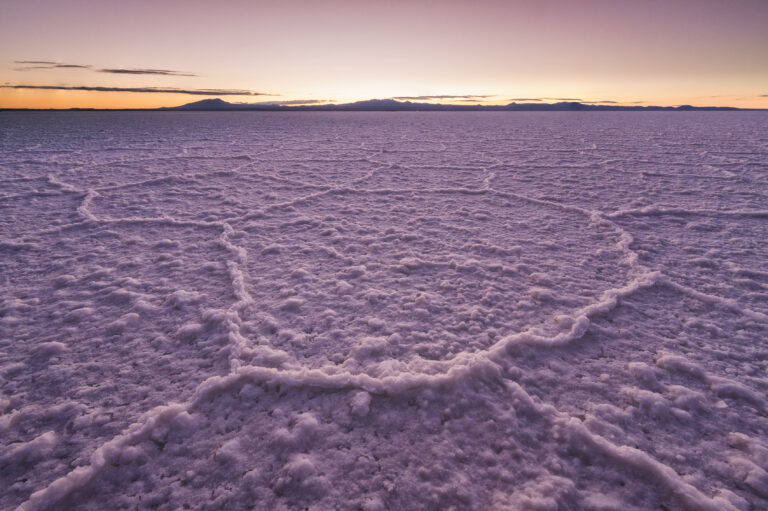 Salar de Uyuni al atardecer con montañas de fondo, salares cristalizados en primer plano