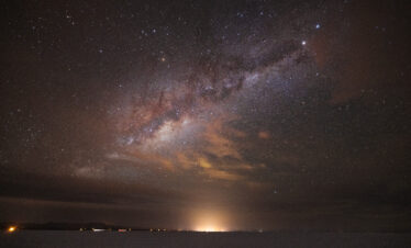 Vía Láctea sobre el Salar de Uyuni con reflejo de luces en el horizonte nocturno