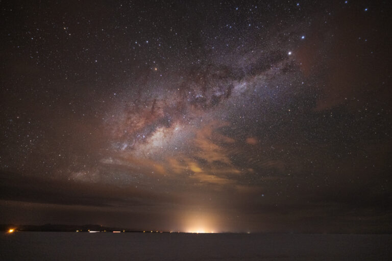 Vía Láctea sobre el Salar de Uyuni con reflejo de luces en el horizonte nocturno