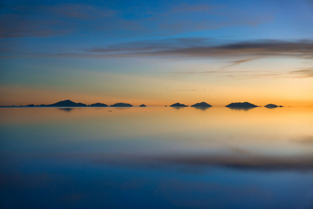 Islas rocosas reflejadas en aguas espejadas del Salar de Uyuni al atardecer con cielo anaranjado