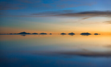 Islas rocosas reflejadas en aguas espejadas del Salar de Uyuni al atardecer con cielo anaranjado