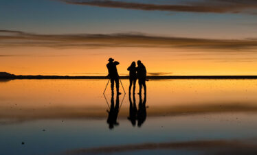 Siluetas de fotógrafos y turistas en el Salar de Uyuni al atardecer, reflejados en el espejo de agua salada